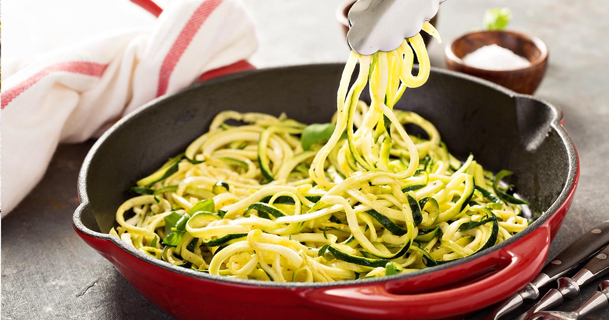 Raw veggie noodles in a red skillet.