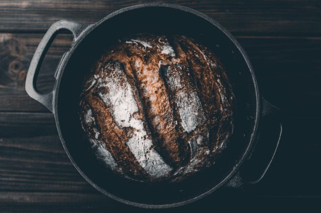 A loaf of bread in a cast iron Dutch oven on a wooden table.
