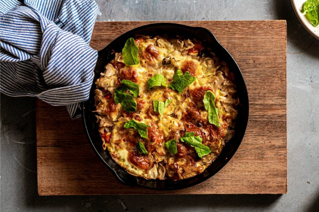 A cast iron skillet with vegetables and herbs on a wooden cutting board.