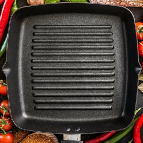 A cast iron grill pan with vegetables and spices on a black background.
