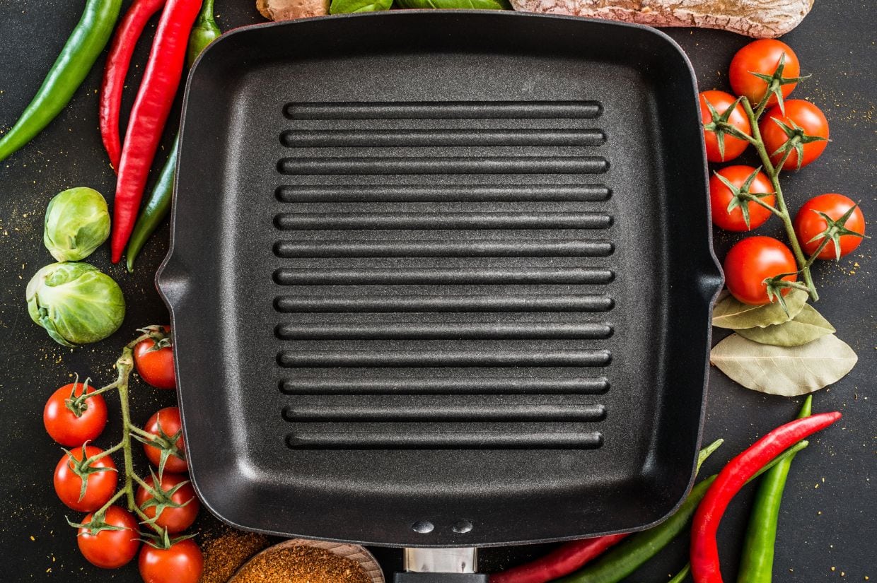 A cast iron grill pan with vegetables and spices on a black background.
