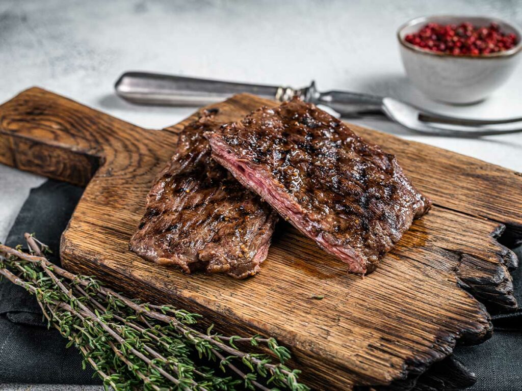 Grilled steak on a cutting board with herbs.