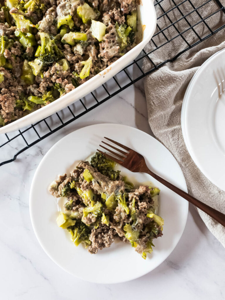 A plate of broccoli and meat casserole with a fork, baked casserole in dish cooling on rack.