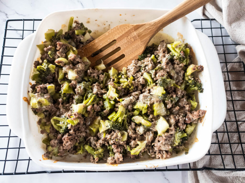 A wooden spatula scooping out of a casserole dish with broccoli and ground beef in it.