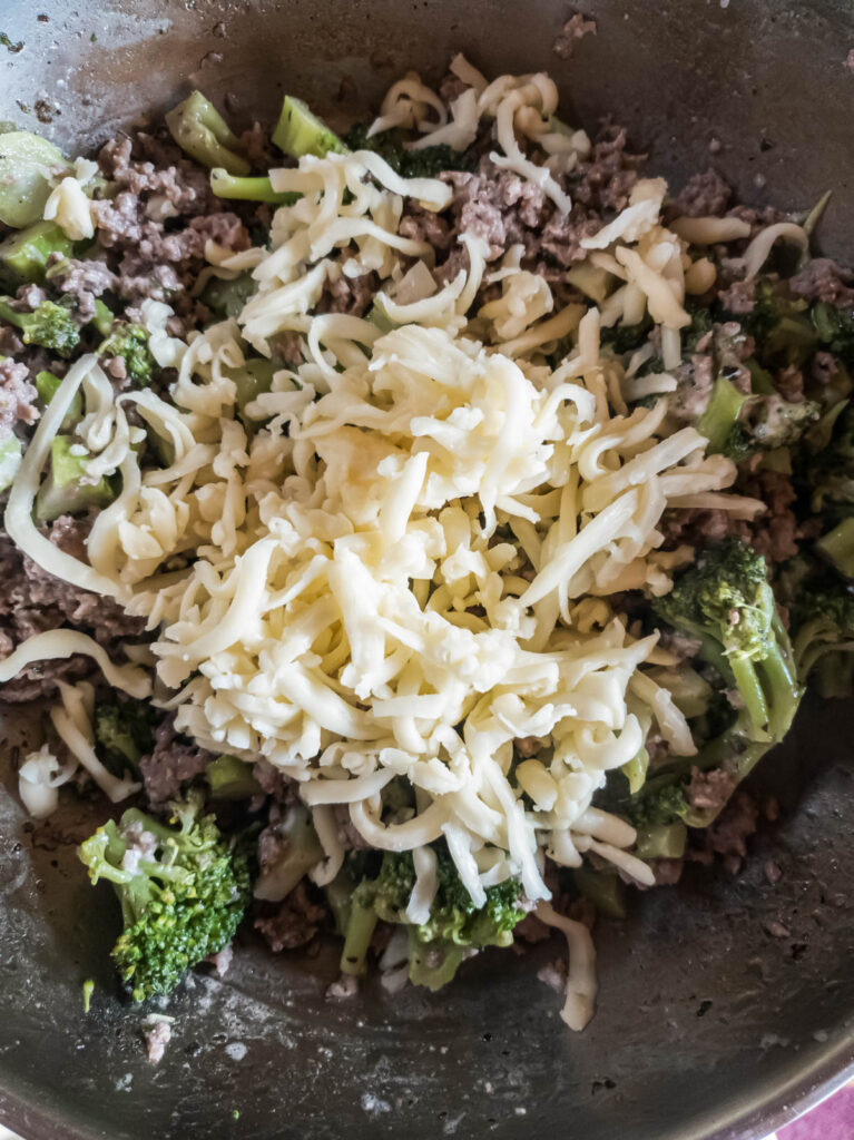 A skillet filled with broccoli, meat and cheese.