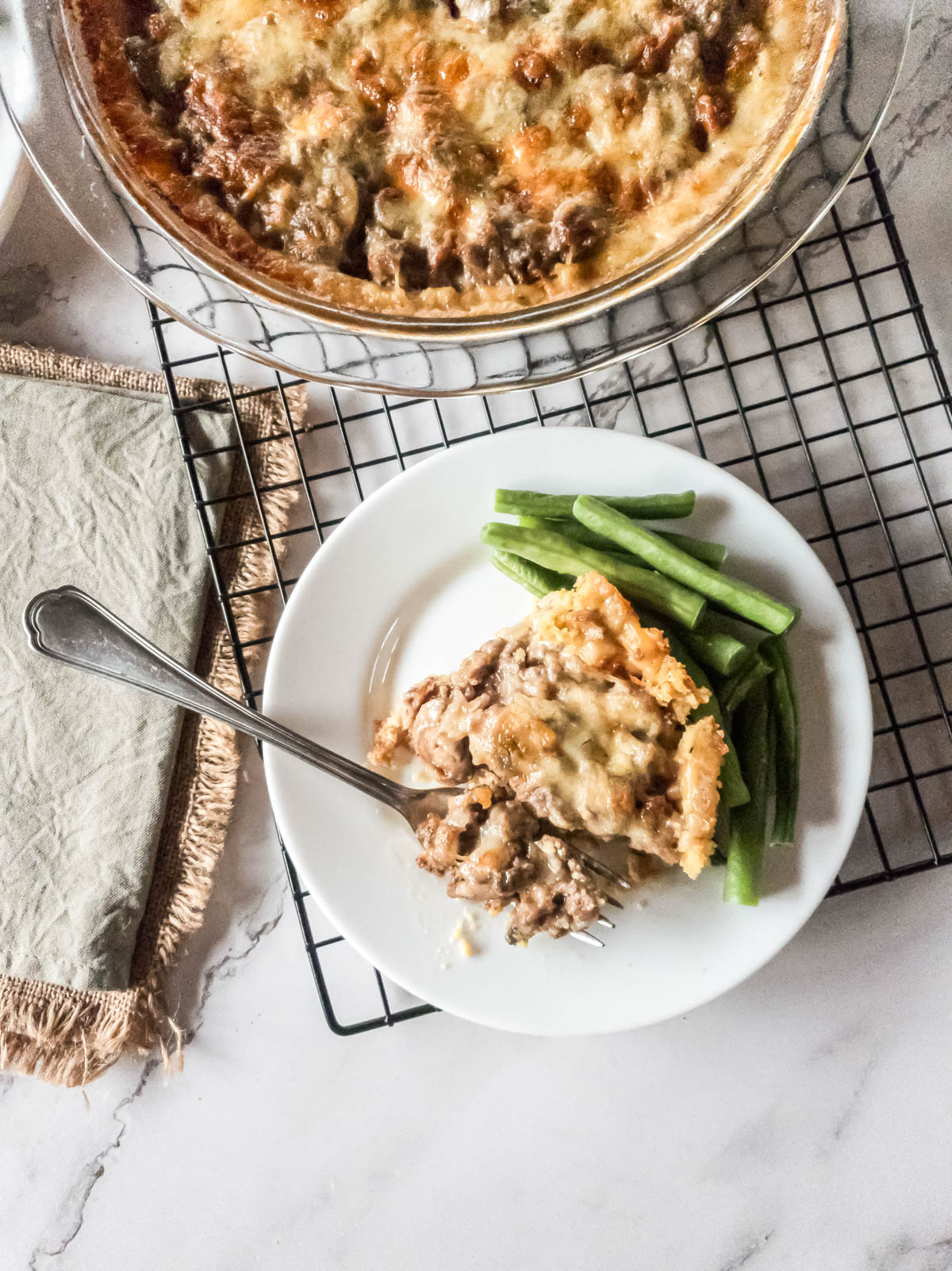 View on meat pie served on a plate next to the pie cooling on a rack.