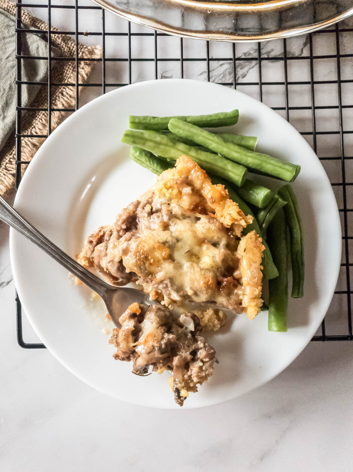 A keto meat pie with green beans on a plate with a fork taking a bite.