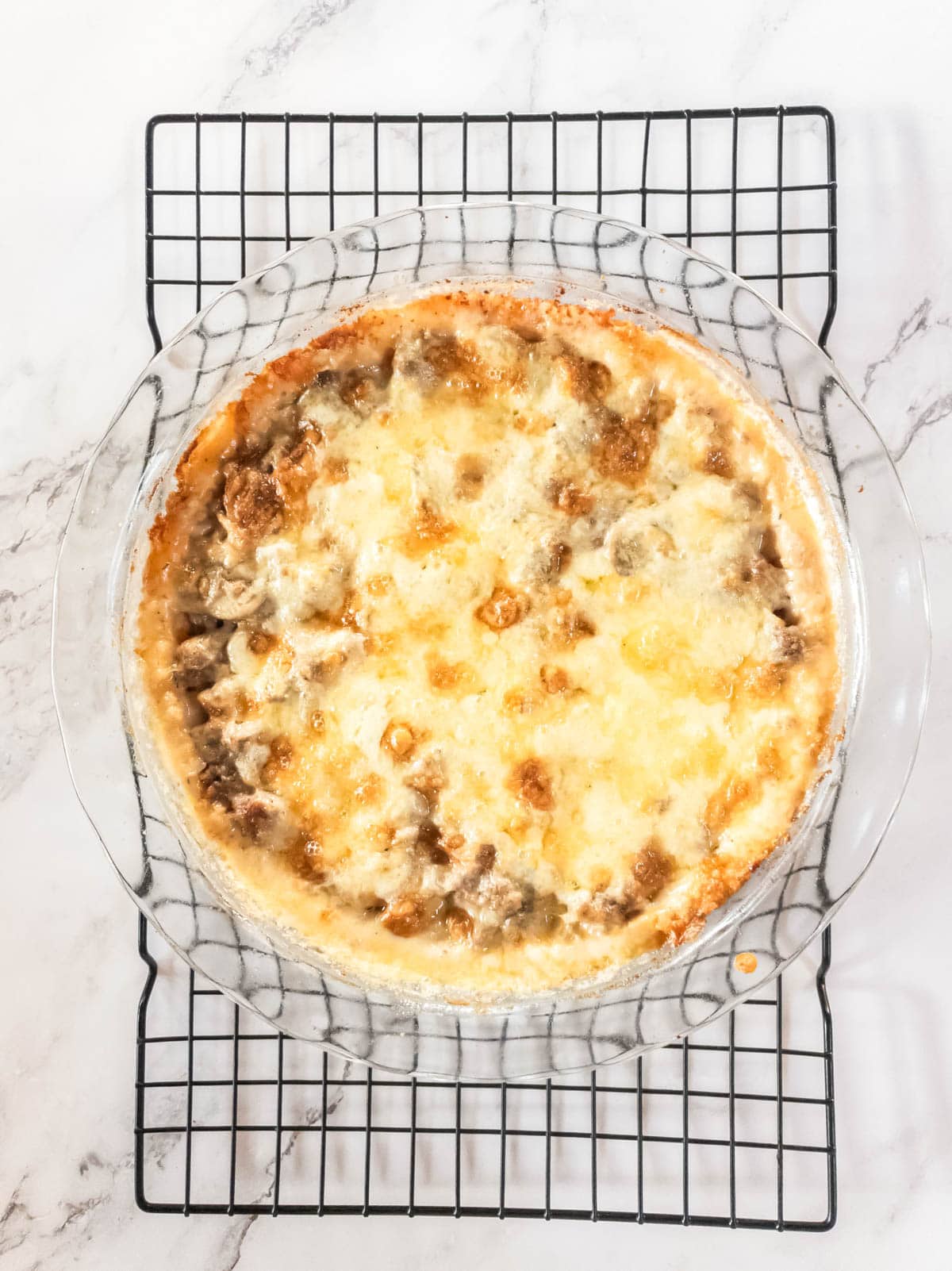 Baked cheesy meat pie cooling on a wire rack.