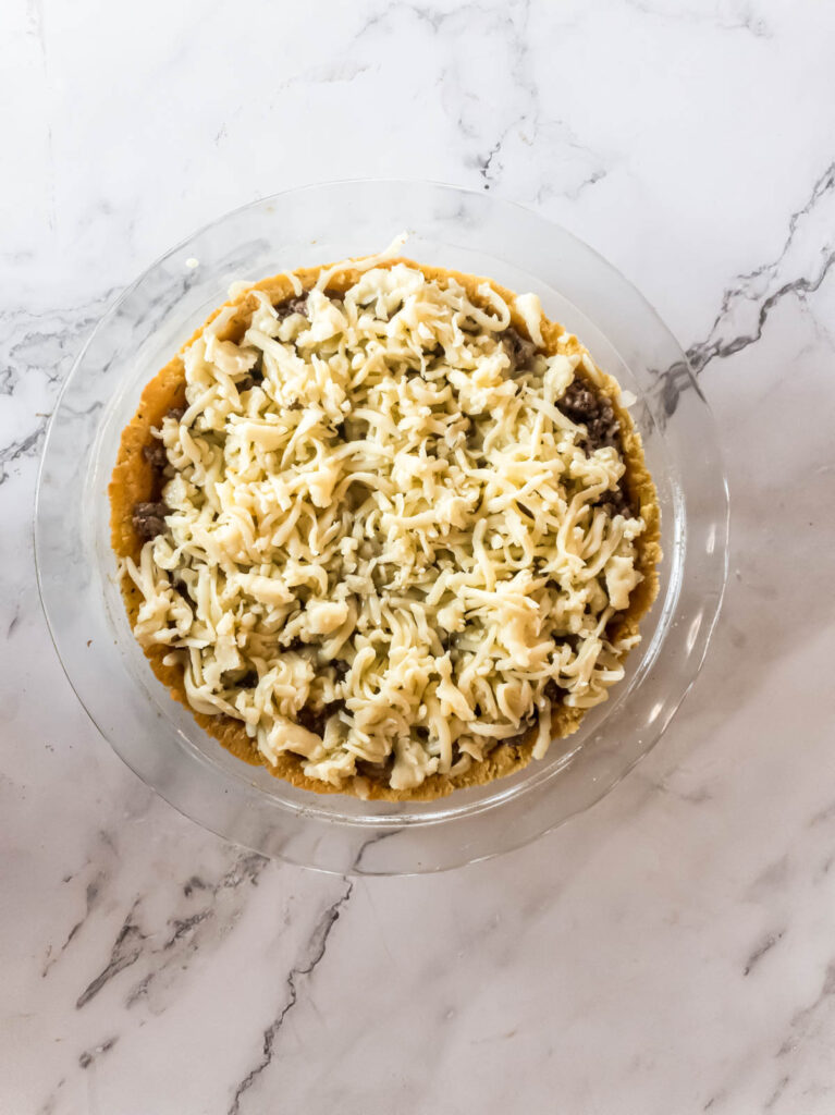 Topping the meat pie with shredded cheese before baking in oven.