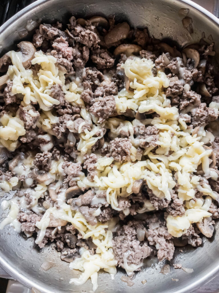 Ground beef, mushrooms, and cheese cooking in a skillet.