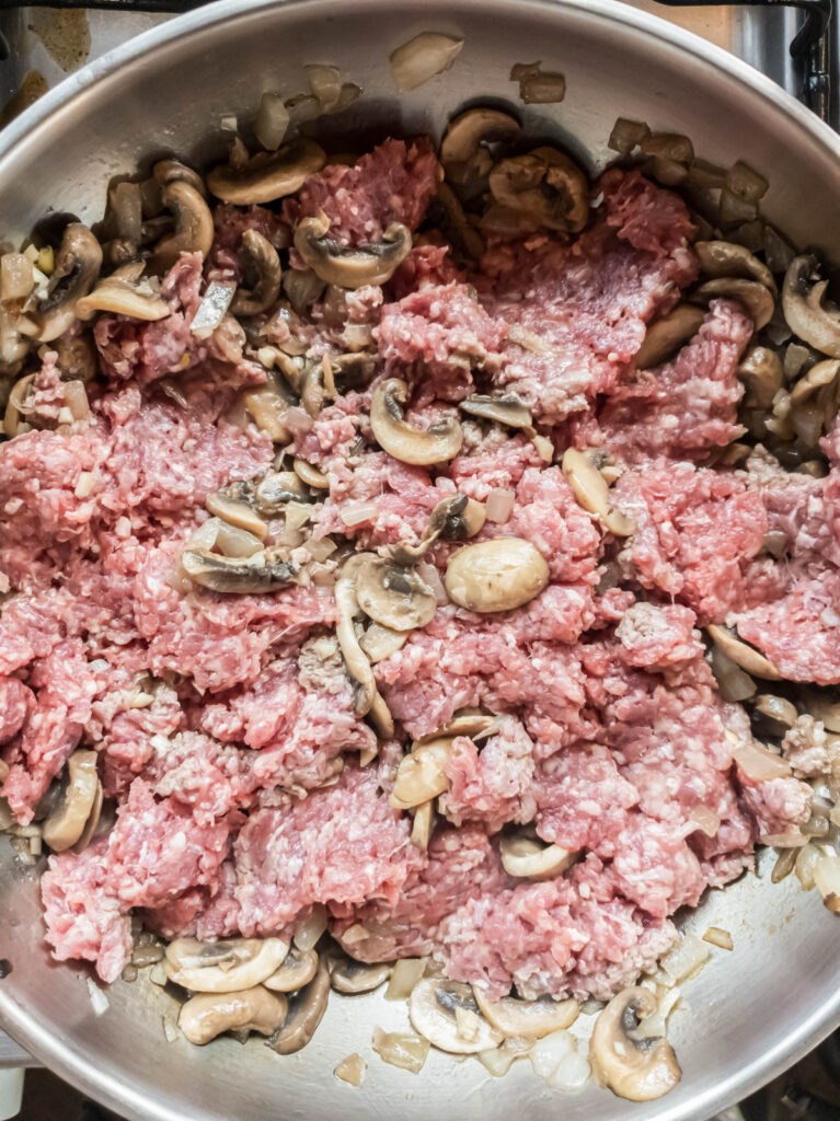 Ground beef mixed with mushrooms cooked on stove.