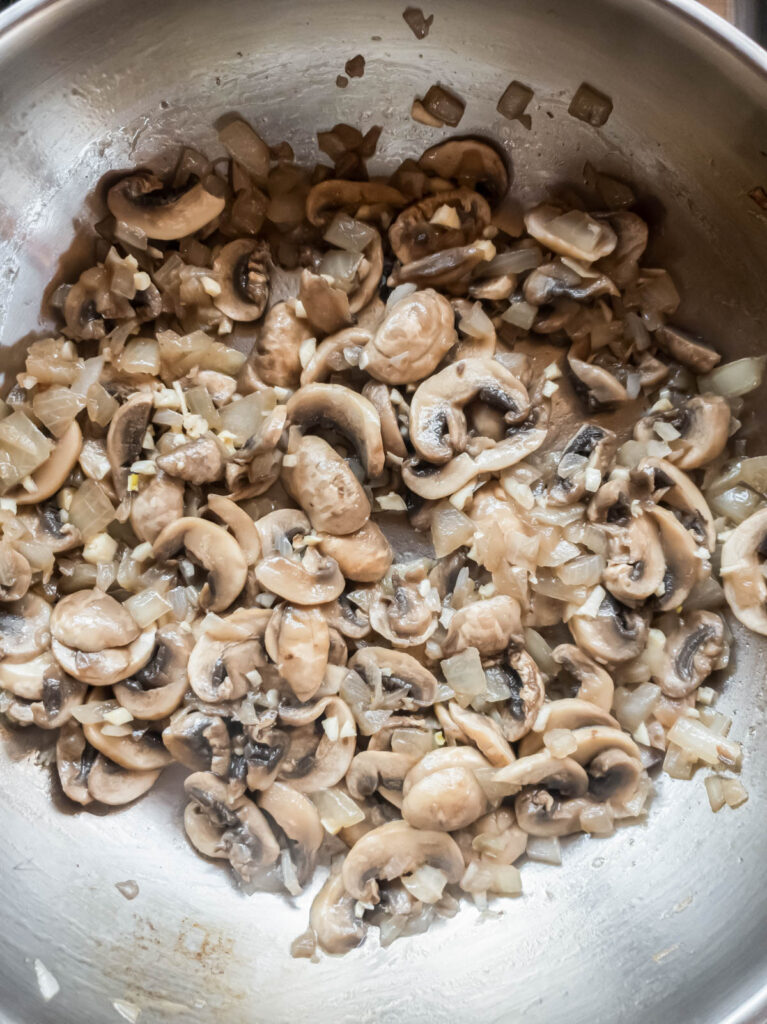 Mushrooms and onions sautéed in a pan on a stove.