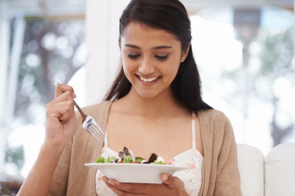 A woman is following an elimination diet and is eating a salad with a fork.