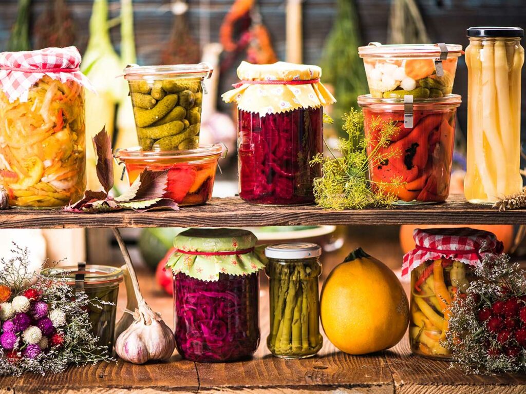 Many jars of pickles and fermented vegetables on a wooden table.