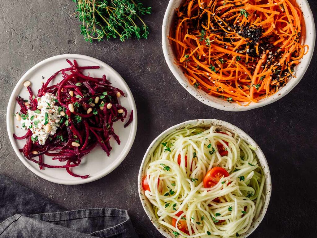 Three bowls of vegetable noodles made from carrots, beets and zucchini.