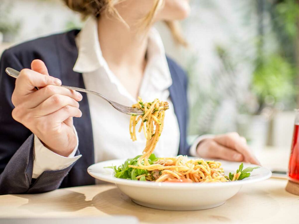 A woman is eating a bowl of pasta with a fork.