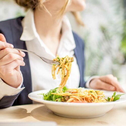 A woman is eating a bowl of pasta with a fork.