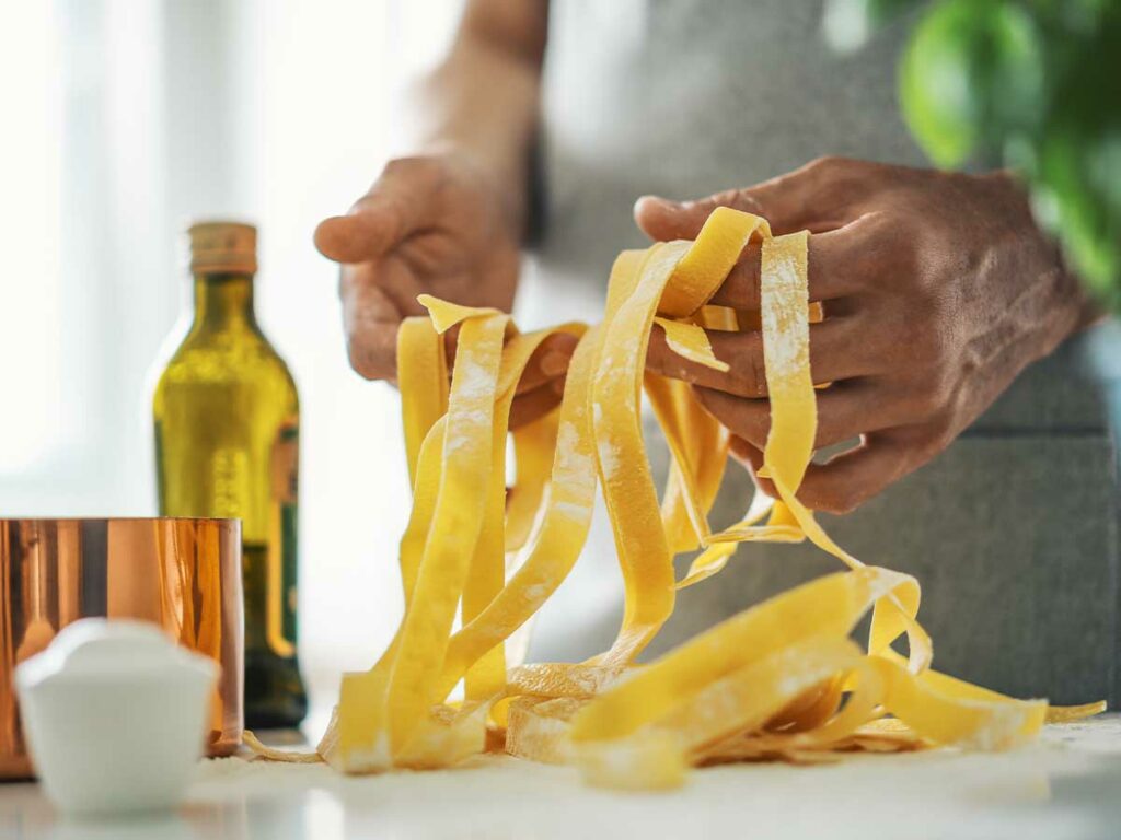 A man is preparing tagliatelle noodles on a kitchen counter.
