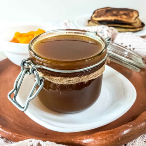 A jar of pumpkin syrup on a plate next to low-carb pancakes.