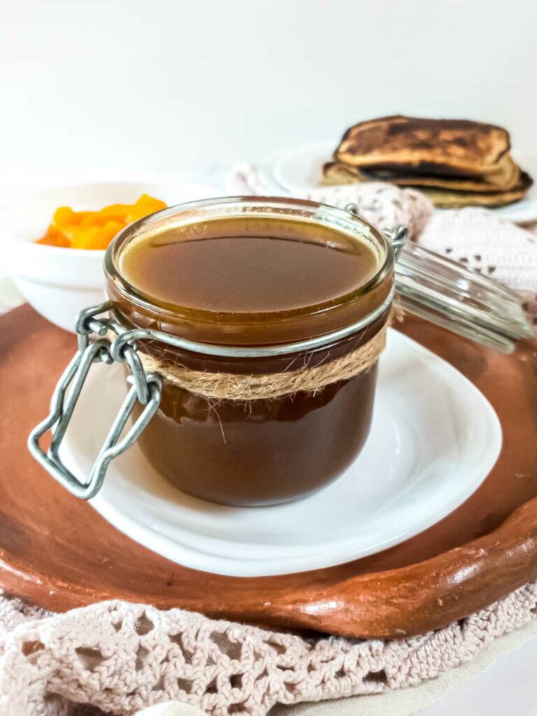 A jar of pumpkin spice syrup on a plate next to low-carb pancakes.