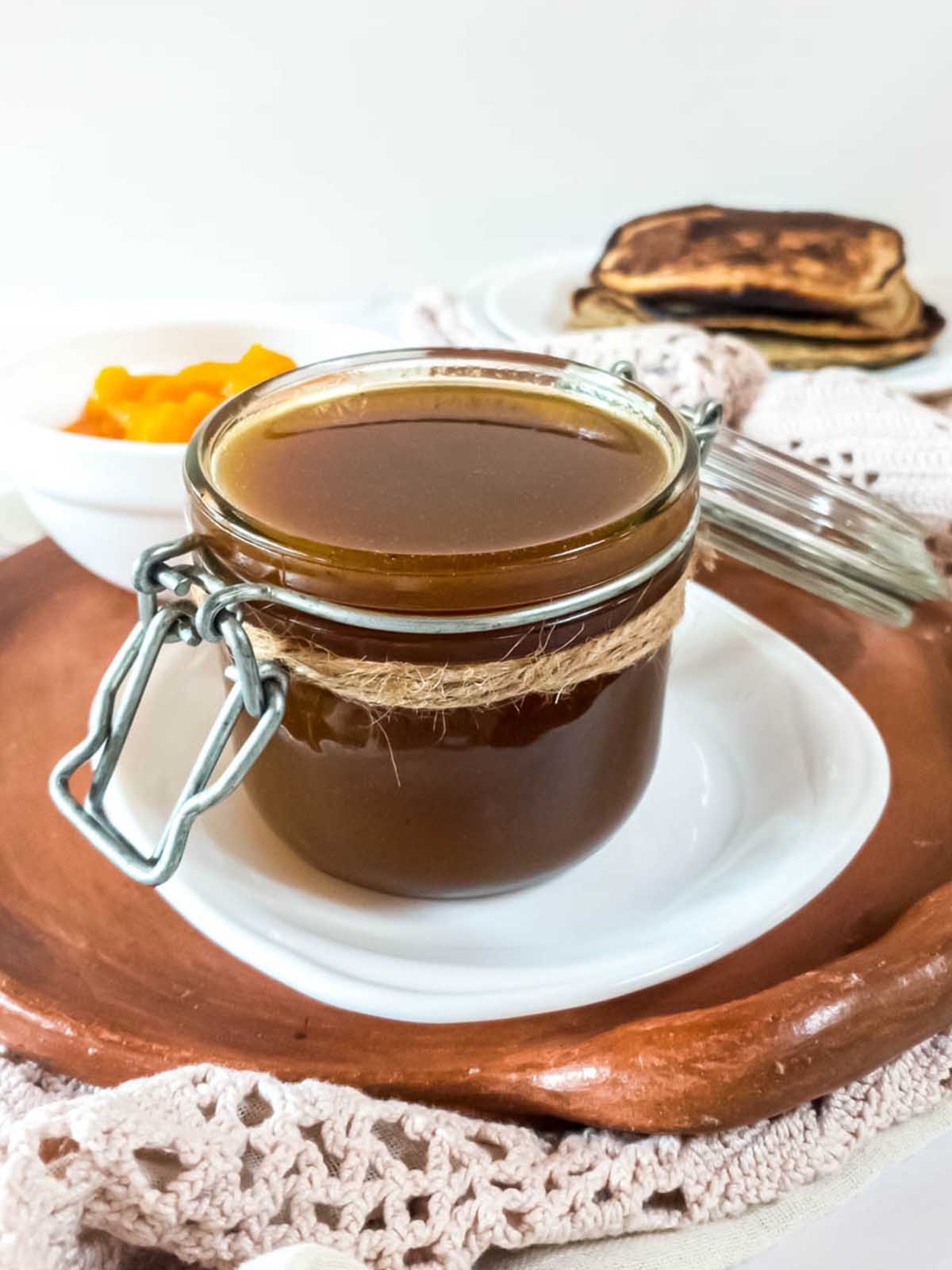 A jar of pumpkin syrup on a plate next to low-carb pancakes.