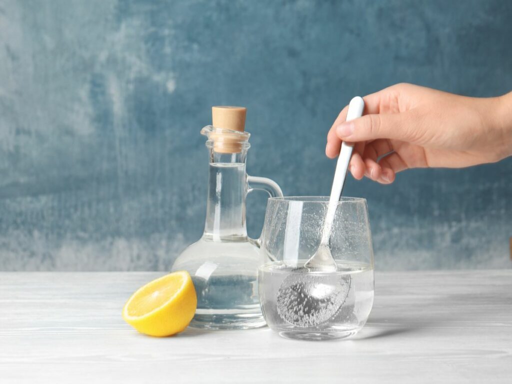 A person pouring vinegar and water into a glass with a lemon in it.