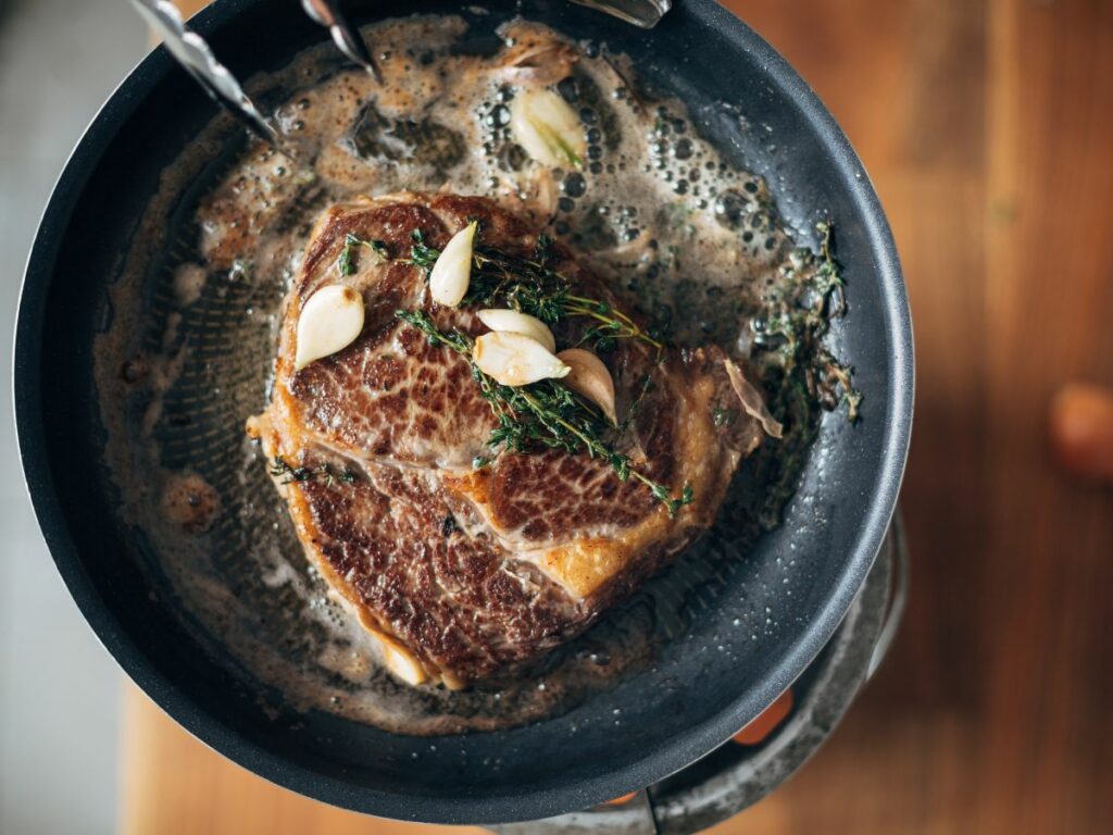 A steak is being cooked in a frying pan.