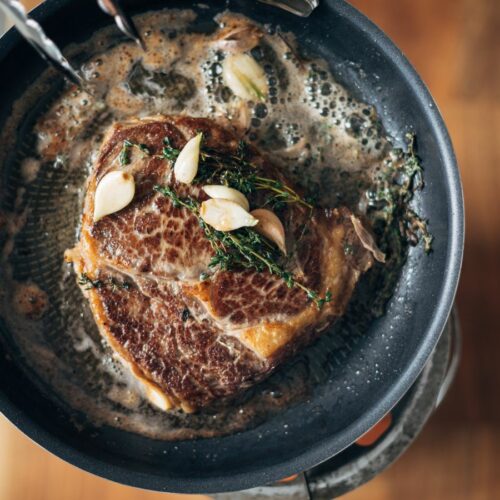 A steak is being cooked in a frying pan.