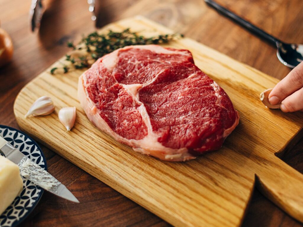 A person cutting a raw piece of steak on a cutting board.