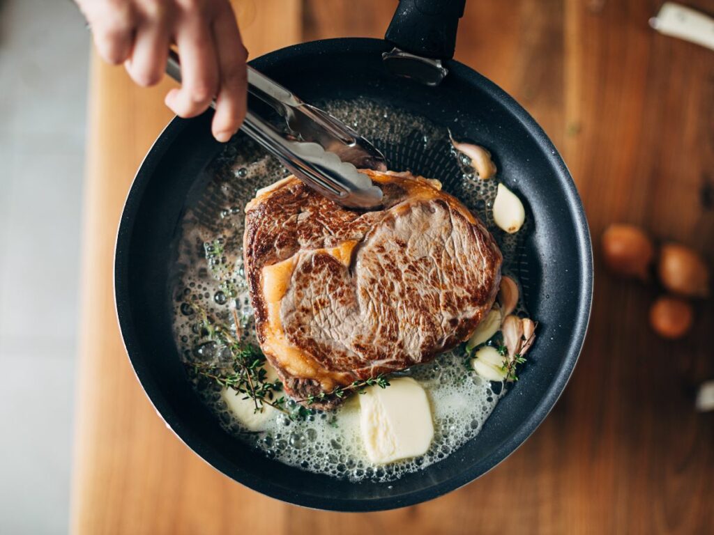 A person searing a steak in a frying pan.
