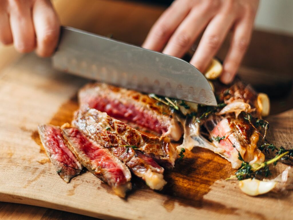 A person slicing a piece of steak on a cutting board.
