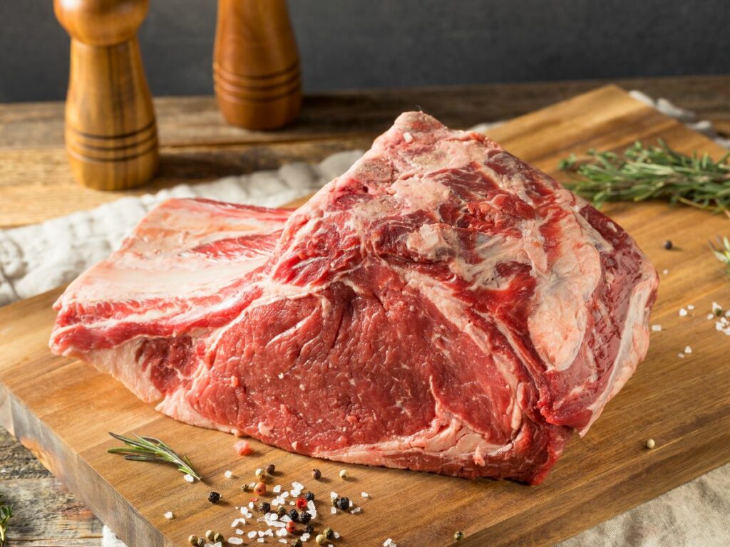 A rib roast on a wooden cutting board with spices.