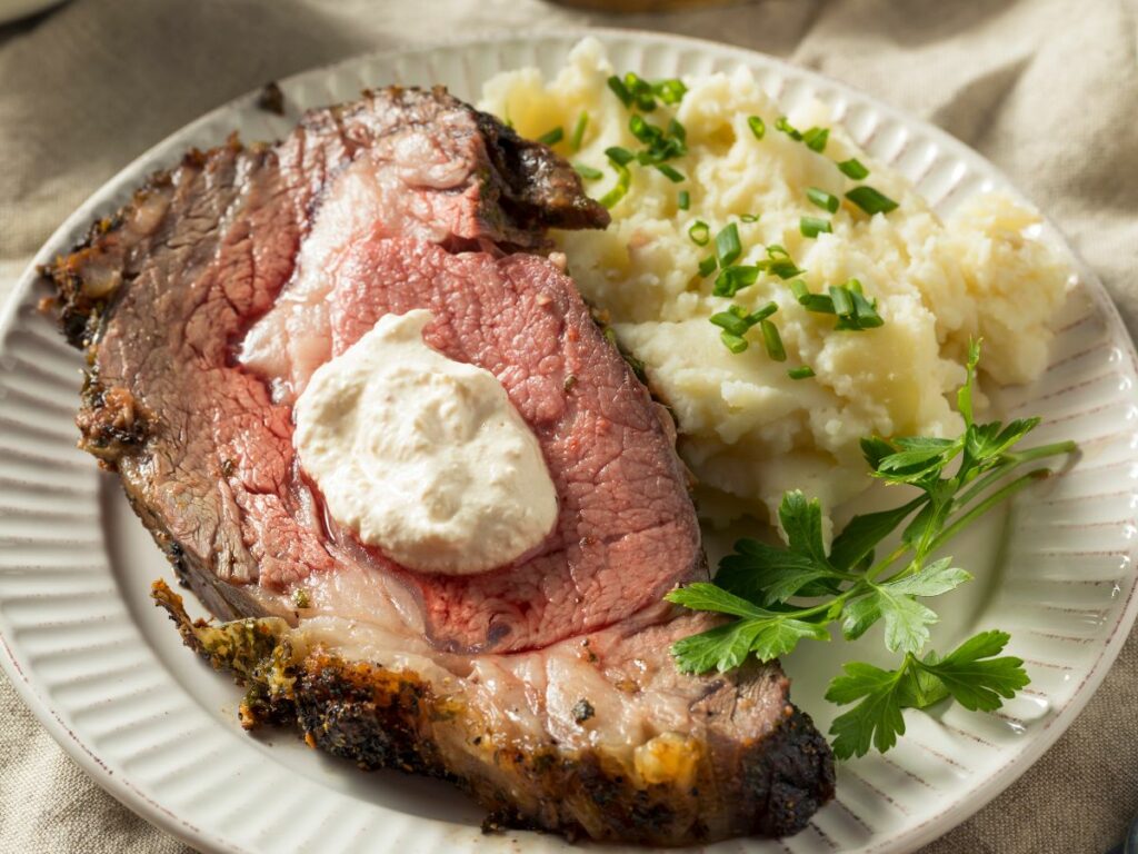 A plate of roast beef with mashed potatoes and sour cream.