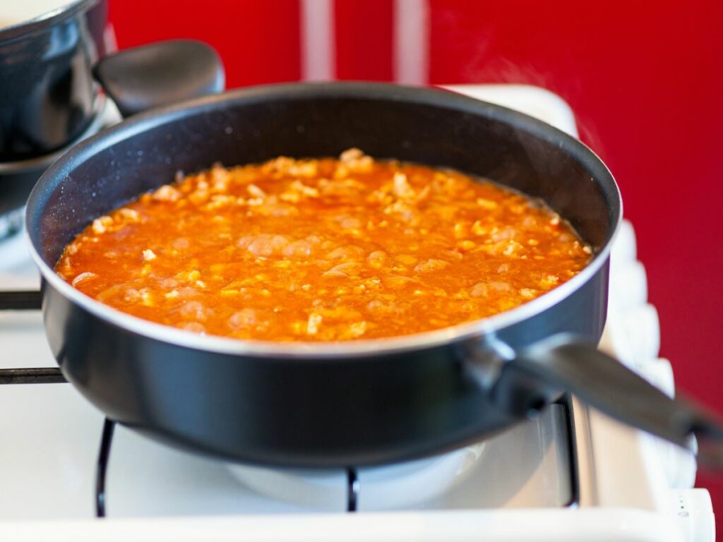 A pot of food cooking in a saute pan on a stove top.
