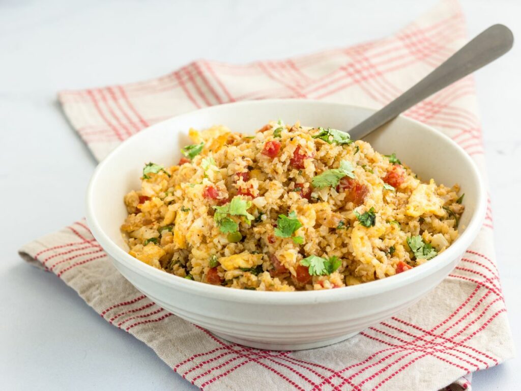 A bowl of cauliflower rice with tomatoes and herbs.