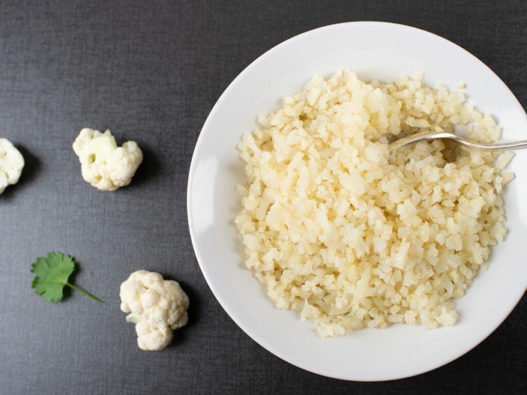 Cauliflower rice in a white bowl with a spoon.