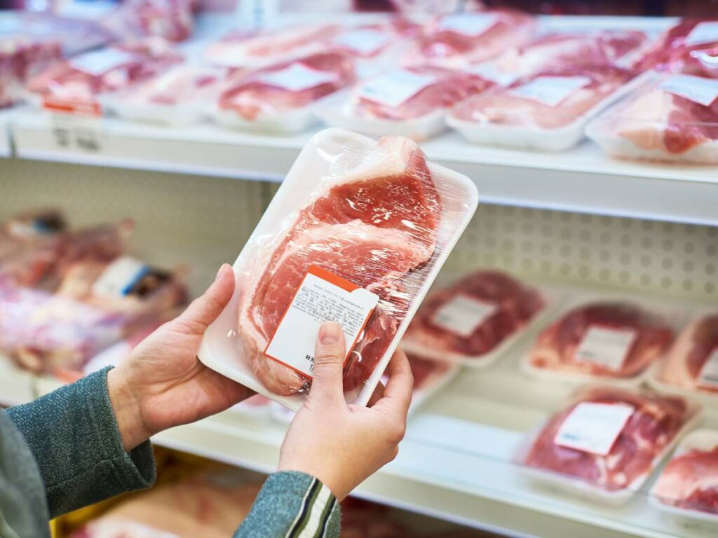 A person is holding a tray of meat in a store.