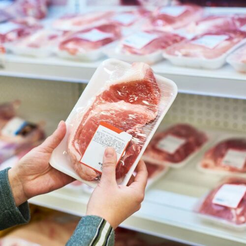 A person is holding a tray of meat in a store.