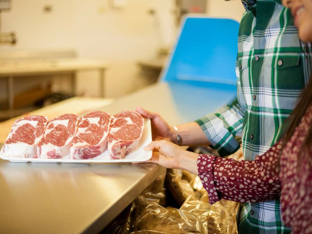 A man and woman picking up tray of meat on a budget.