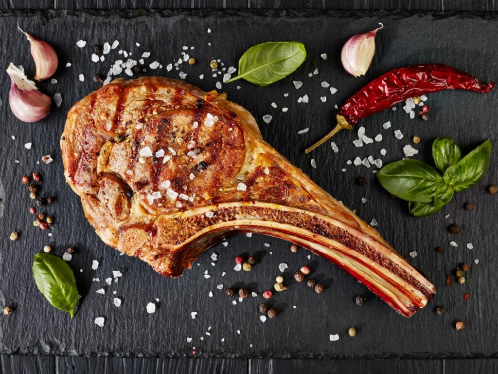 A grilled steak with spices and herbs on a black background.