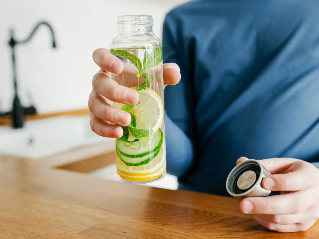 A man holding a glass bottle of water with cucumbers and lemons.