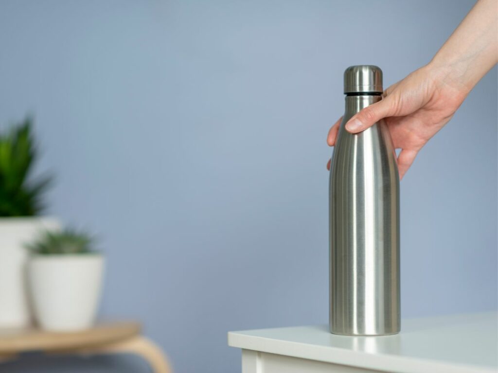A person holding a stainless steel water bottle on a table.