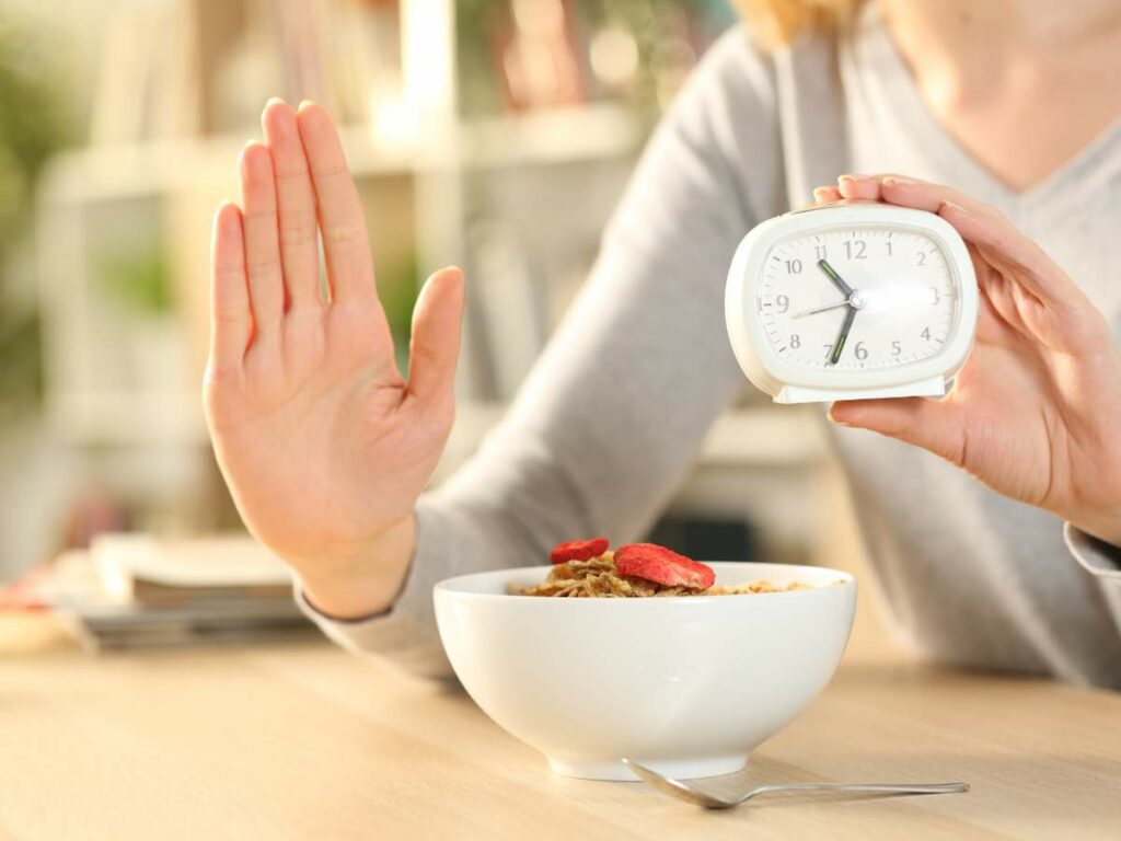 A woman holding an alarm clock and a bowl of cereal.