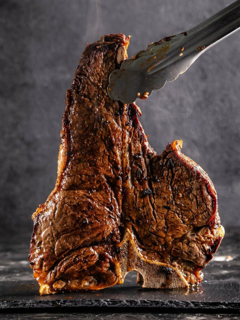 A t-bone steak is being cut with a knife on a dark background.