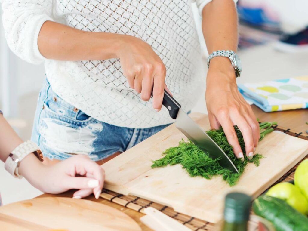 Two women chopping vegetables on a cutting board.