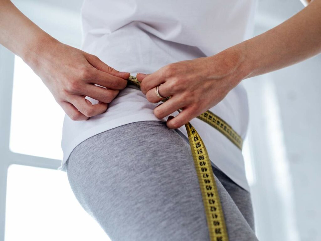 A woman is measuring her waist with a measuring tape.