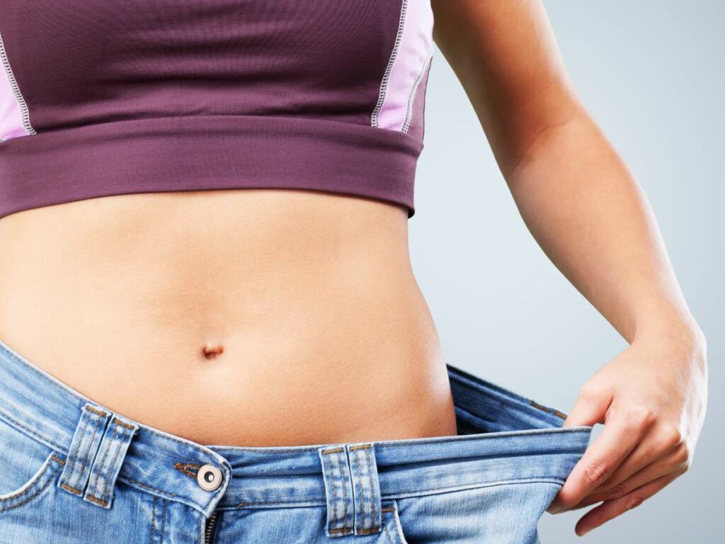 A woman is holding her jeans away from her stomach because she lost weight.