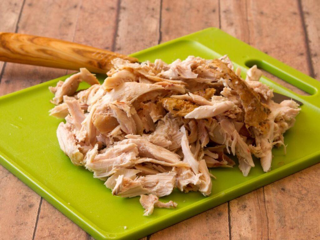 Shredded chicken on a green cutting board.