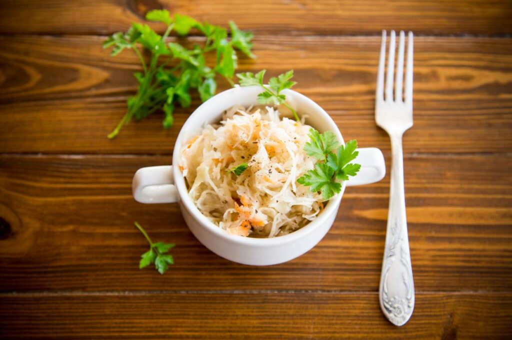 A white bowl with sauerkraut and a fork on a wooden table.