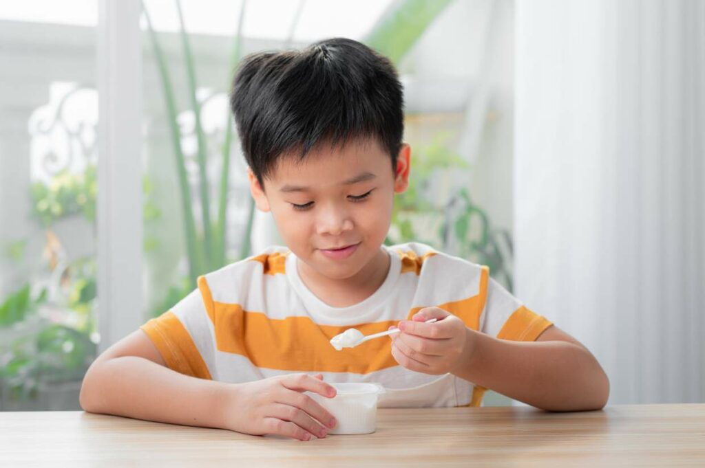 A young boy eating a spoon of yogurt.